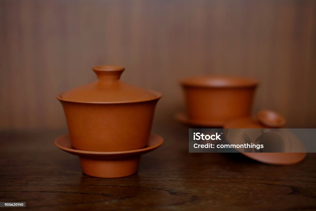 TWO CHINESE TEA SETS Two chinese tea sets made from clay composed of cups, lids and saucers, focus at the front one. They are set on the wood table in front of  wood wall. Antique Stock Photo