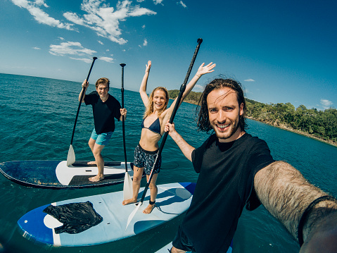 Three friends taking a selfie while paddle boarding.