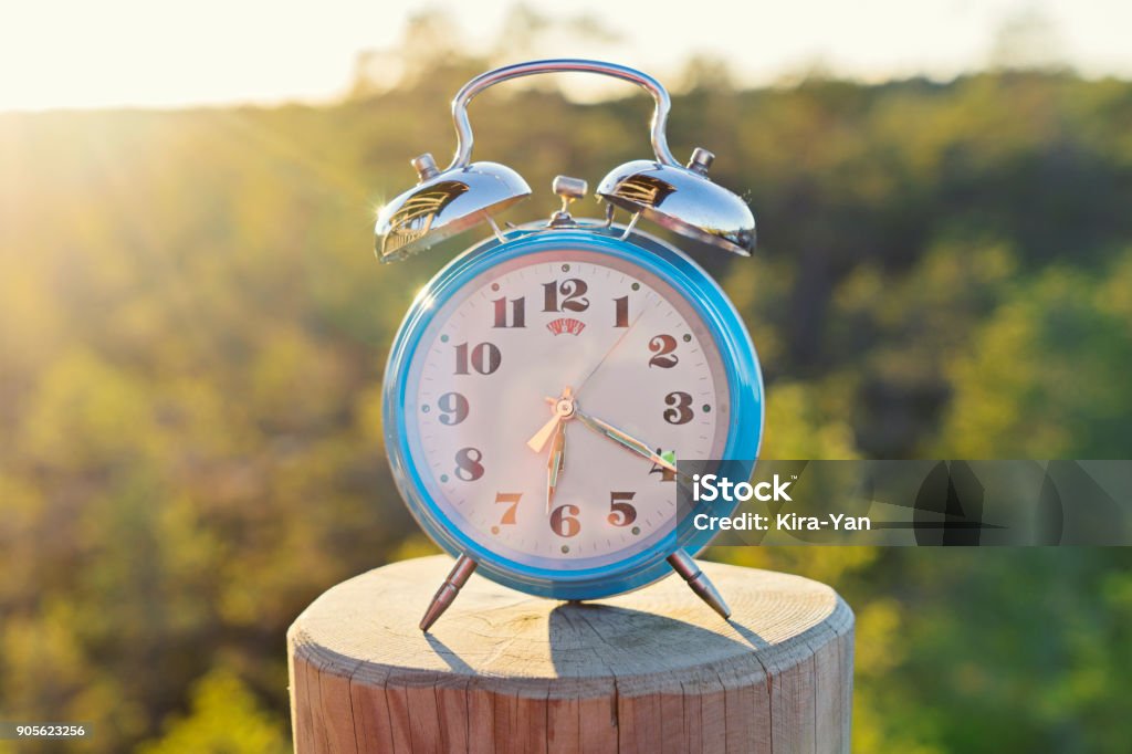 Vintage blue alarm clock on summer forest background Vintage blue alarm clock on summer forest background. Daylight saving time concept winter time Time Stock Photo