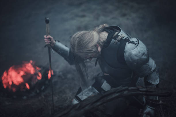 ragazza a immagine di giovanna d'arco in armatura e con la spada tra le mani inginocchiata sullo sfondo di fuoco e fumo. - jeanne foto e immagini stock