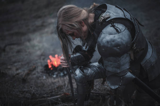 ragazza a immagine di giovanna d'arco si inginocchia in armatura e con la spada tra le mani sullo sfondo di fuoco e fumo. - jeanne foto e immagini stock