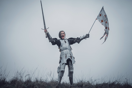 Chica en la foto de Jeanne d ' Arc se encuentra en armadura y temas grito de la batalla con la espada hacia arriba y bandera en sus manos. photo