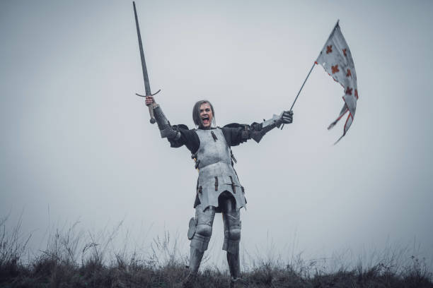 dziewczyna na zdjęciu jeanne d'arc stoi w zbroi i problemy okrzyk bojowy z mieczem podniesiony i flagi w jej rękach. - jeanne zdjęcia i obrazy z banku zdjęć