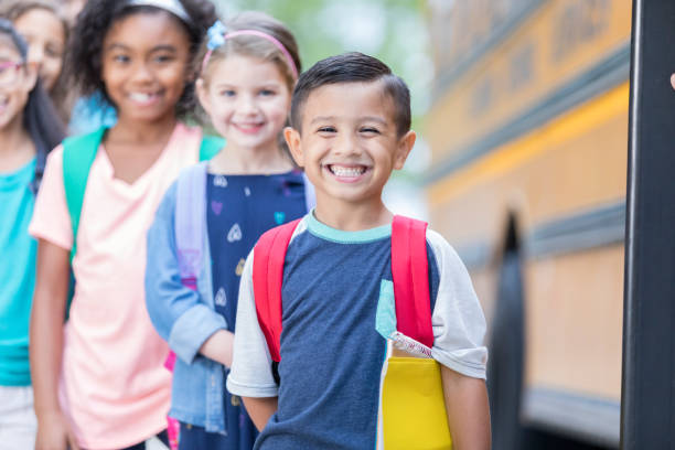 istock Little boy smiles for camera while waiting to board school bus 905633208