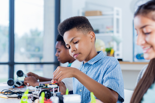 A preteen boy works alongside classmates as he finishes his robotics project at school.
