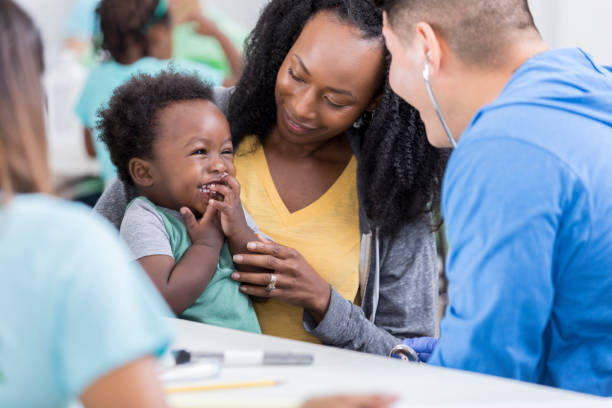 Male pediatrician examines baby boy in free clinic Caring male doctor smiles while talking to a baby boy in a free clinic. The boy's mom is holding him. community center photos stock pictures, royalty-free photos & images
