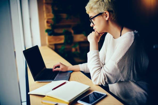 istock Pensive creative manager in eyeglasses reading news on laptop analyzing information for report, skilled female copywriter in eyewear concentrated on remote job preparing publication for web page 905637880