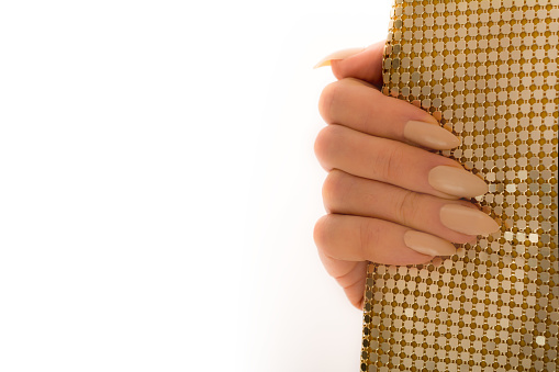 Mature woman showing her beige colored stiletto manicure with gold sequin clutch