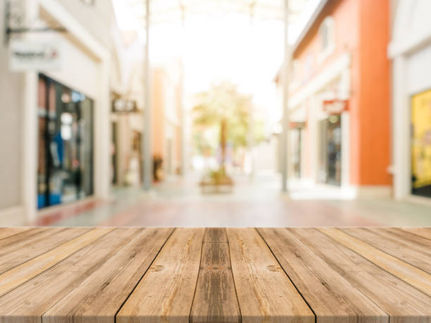 istock Wooden board empty table blurred shopping mall background. Perspective brown wooden table blur in department store background - can be used for display or montage your products. Mock up for of product 905643554