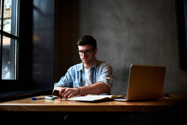 istock Professional designer dressed in denim shirt holding telephone in hand while working on new graphic project during working process sitting in own studio with laptop computer connecting to wireless internet 905653710