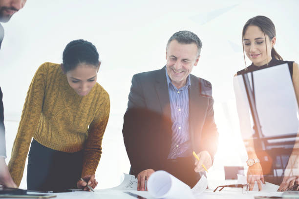 istock Smiling crew of architects satisfied with accomplished blueprint for project drafting together in office.Mature boss checking work of experienced engineers cooperating with employees in good mood 905663128