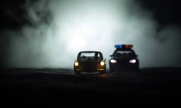Toy BMW Police car chasing a Ford Thunderbird car at night with fog background. Toy decoration scene on table . Selective focus "u2013 11 JAN 2018, BAKU AZERBAIJAN