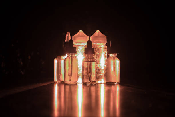 istock Vape concept. Smoke clouds and vape liquid bottles on dark background. Light effects 905671314