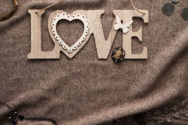 Wooden lettering Love. Woolen cloth. Earrings, rings, brooch decomposed. Brown background color. A warm cozy atmosphere. A symbol of love. Valentine's day. Design element.