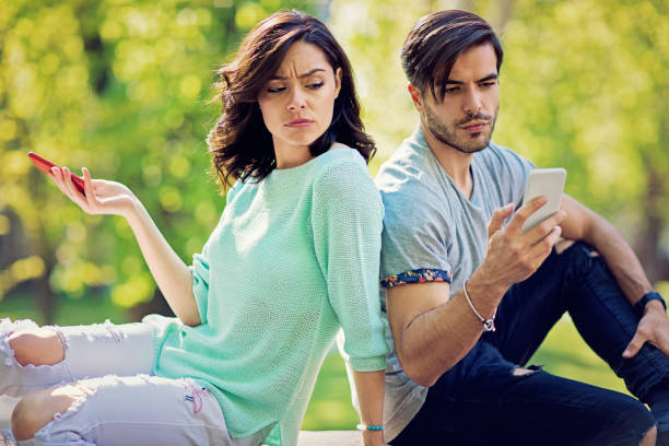 couple in conflict is texting in the park and sulking each other - inveja imagens e fotografias de stock