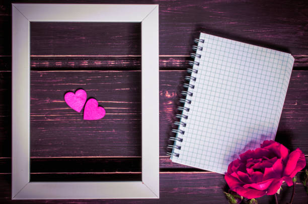 istock blank photo frame with two hearts , blank notebook with copyspace and pink rose flowers on wooden background. greeting card and holiday concept. 905686964