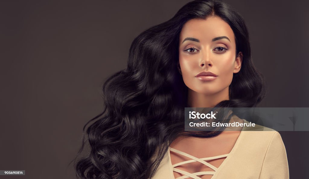 Black haired woman with voluminous, shiny and curly hairstyle.Frizzy hair. Young black haired woman  with voluminous, shiny and wavy hair . Beautiful model with long, dense and curly hairstyle. Frizzy hair. Hair Stock Photo