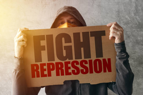 istock Hooded activist protestor holding Fight repression protest sign 905703386