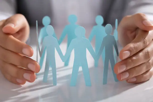 Photo of Businessperson Hand Protecting Paper Cut Out Figure On Table