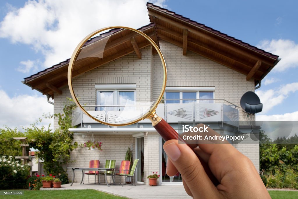 Person's Hand Holding Magnifying Glass Over Luxury House Close-up Of Person's Hand Holding Magnifying Glass Over Luxury House Outdoors Examining Stock Photo