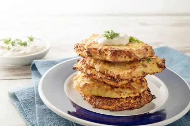 pile of golden crisp vegetables rosti from cauliflower and parmesan cheese with a creamy dip and parsley garnish on a blue napkin and a light wooden background, copy space, selected focus, narrow depth of field