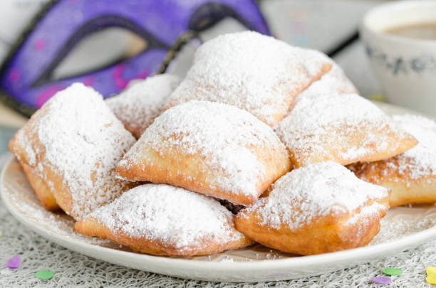 Traditional New Orleans beignets served for Mardi Gras Homemade New Orleans style beignets are small squares of fried dough covered in powdered sugar prepared for Mardi gras. Served on a plate with cup of coffee,mask and confetti beignet stock pictures, royalty-free photos & images
