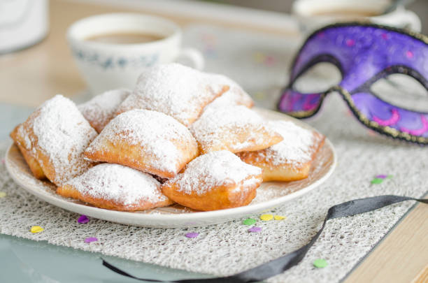 Traditional New Orleans beignets served for Mardi Gras Homemade New Orleans style beignets are small squares of fried dough covered in powdered sugar prepared for Mardi gras. Served on a plate with a cup of coffee,mask and confetti fritter photos stock pictures, royalty-free photos & images