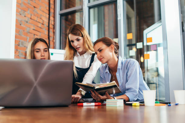 istock Three female college students doing homework together using one laptop and lecture notes sitting at desk in study room 905731188