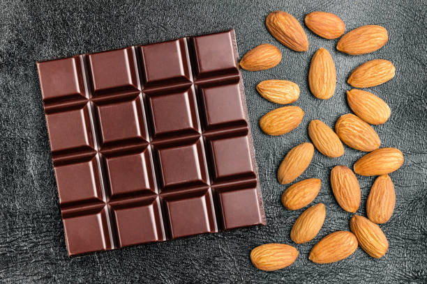 istock Dark, bitter chocolate bar and almond nuts on black leather texture background, top view 905731448