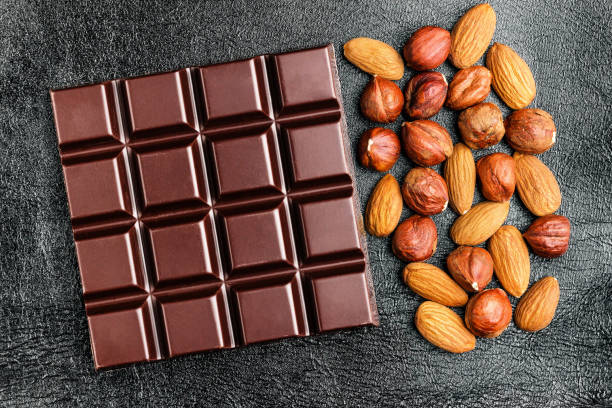 istock Dark, bitter chocolate bar, almond and hazelnut on black leather texture background, top view 905731544