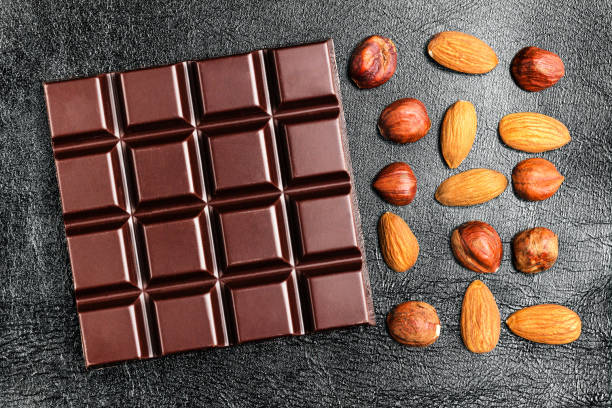 istock Dark, bitter chocolate bar, almond and hazelnut on black leather texture background, top view 905731622