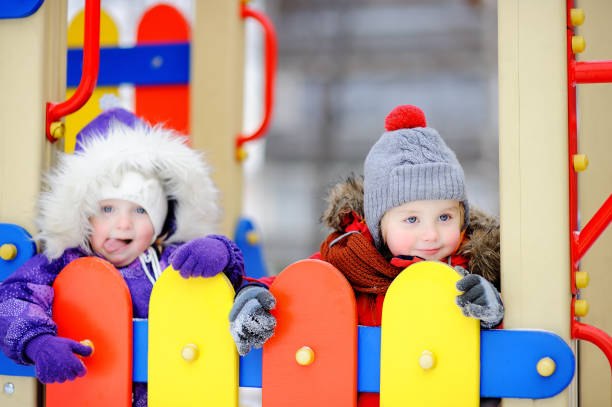 menino e uma menina em roupas de inverno se divertindo no parque infantil ao ar livre - playground snow winter little girls - fotografias e filmes do acervo