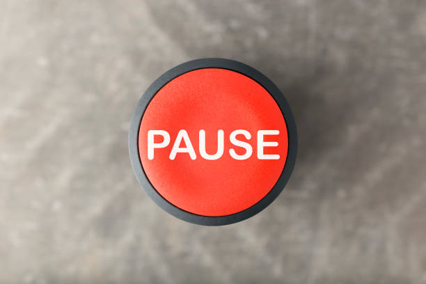 Overhead of a red pause push button over a blurred gray background