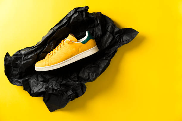Yellow sneaker in black crumpled wrapping paper on yellow background
