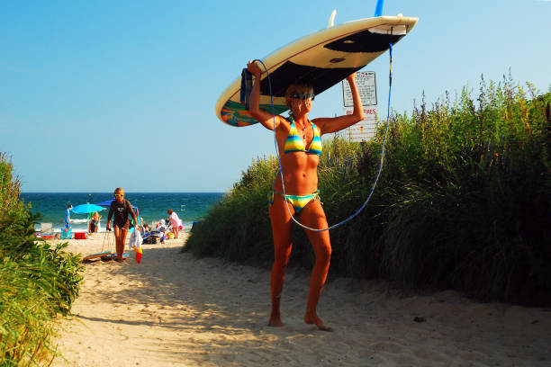 Days End at Ditch Plains Beach, Montauk, Long Island Montauk, NY, USA July 27, 2010 A young woman carriers her surfboard from Ditch Plains Beach in Montauk, New York.  Ditch Plains is considered one of the premier surfing locations on the east coast montauk point stock pictures, royalty-free photos & images
