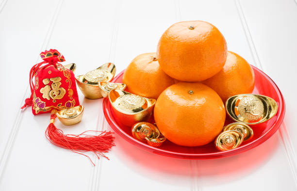 Chinese New year,ang pow red felt fabric bag with gold ingots and tangerine oranges with red tray on white wood table top,Chinese Language mean Happiness and on ingot mean wealthy. stock photo