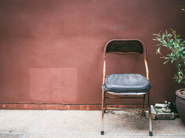istock Old cheap rusty chair with plant by grunge brown wall. 905799332