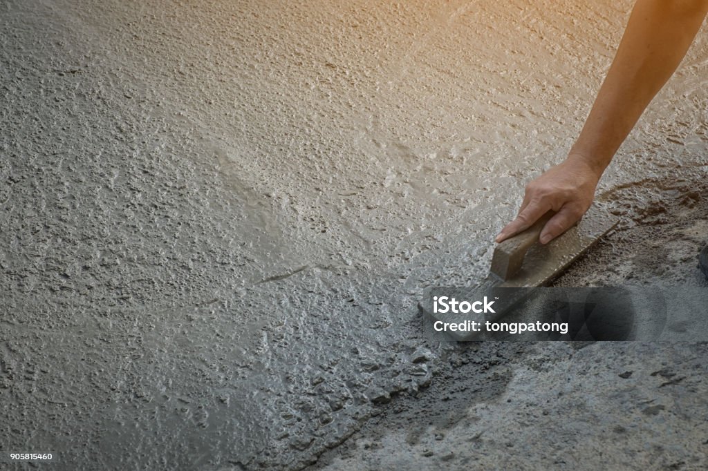 Workers person not wearing dirt boots digging with hoe (shovel) on concrete floor, Construction workers leveling concrete pavement. Upgrade to residential street leveling concrete slab, working place Concrete Stock Photo