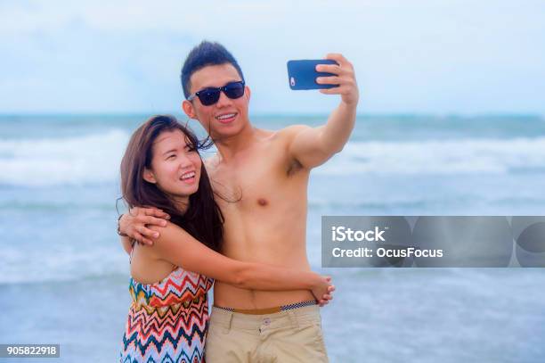 Young Happy And Beautiful Asian Chinese Couple Taking Selfie Photo With Mobile Phone Camera Smiling Joyful Having Fun On The Beach In Romance And Lovers Holidays Trip Picture Concept Stock Photo - Download Image Now