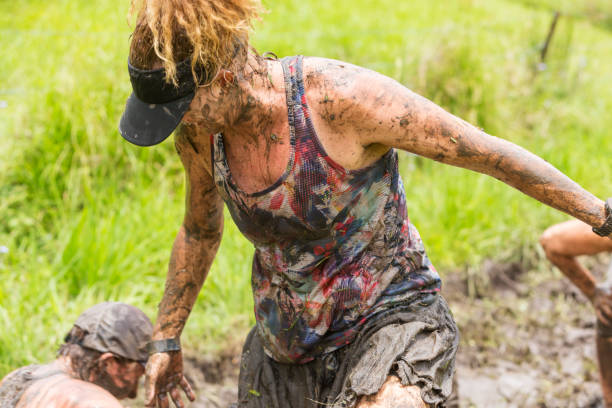 Mud covered mature women having fun competing in a bog on a mud run obstacle course cross country race