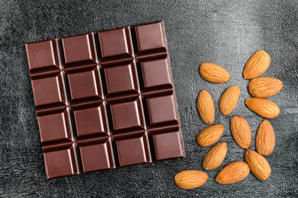 istock Dark, bitter chocolate bar and almond nuts on black leather texture background, top view 905839768