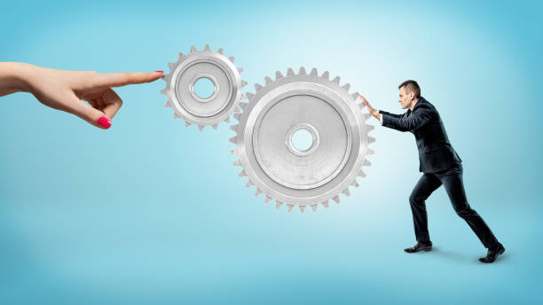 istock A small businessman pushes at a large gear interlocked with a small one while a female finger stops their movement 905848744