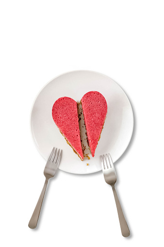 A view from above of a white porcelain plate with two heart-shaped slices of a strawberry tofu cheesecake and two forks on the white background