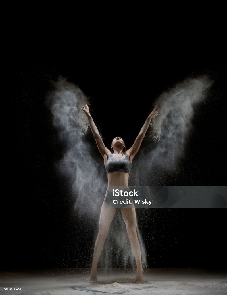 Girl in top and shorts in a white dust cloud shot Slim girl wearing top and shorts in a cloud of white dust shot on black background Acrobat Stock Photo