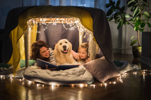 heureuse mère et fille se détendre autour d’un chien dans une tente et lire un livre. - dog family indoors child photos et images de collection