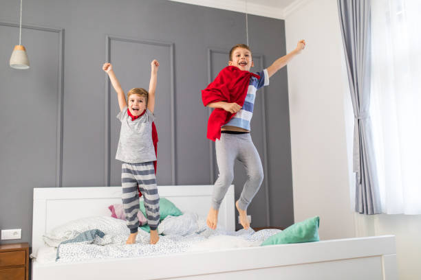 istock Joyful boys playing superheroes while jumping on a bed. 905862170