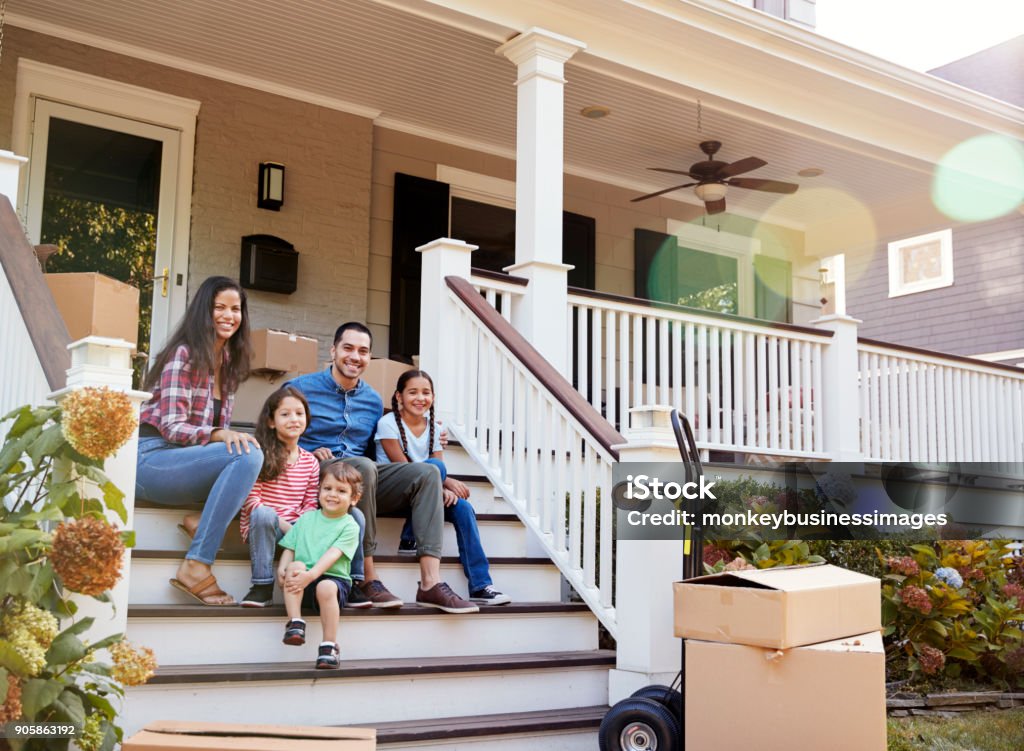 Family Sitting On Steps Of New Home On Moving In Day Home Ownership Stock Photo