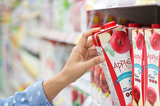 Woman hand choosing to buy apple juice on shelves in supermarket