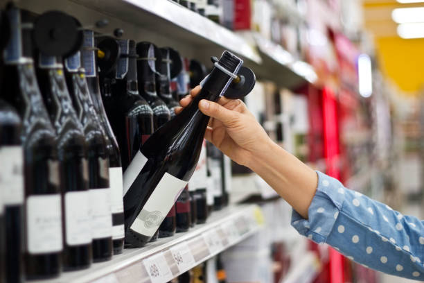 frau kauft eine flasche wein im supermarkt hintergrund - wine bottle bottle burgundy wine stock-fotos und bilder