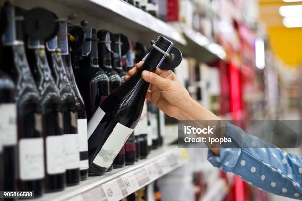 La Donna Sta Comprando Una Bottiglia Di Vino Sullo Sfondo Del Supermercato - Fotografie stock e altre immagini di Alchol